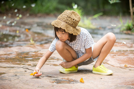 cute little asian girl play with beautiful butterfly with her hand and finger,wearing brown hatの写真素材