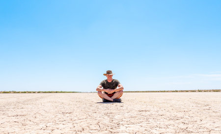 a man sits on dry ground covered with cracks. Tired of heat man sitting in the desert