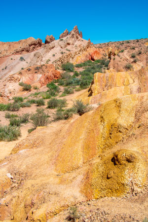 Sharp Mountain is a rock made of red orange stone and clay against a bright blue sky without clouds and desert vegetation in Fairy Tale Canyon Kyrgyzstan, Skazka Canyon.の写真素材