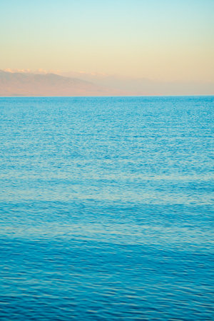 The surface of the water in the Issyk Kul mountain lake in Kyrgyzstan at sunset.Pastel and soft tones of water and sky against the background of mountains.の写真素材