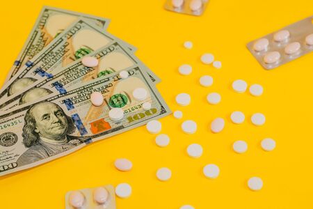 dollars and scattered pills on yellow background close upの写真素材