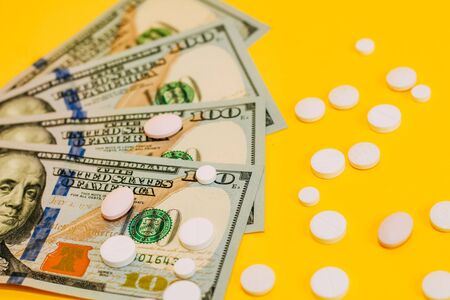 dollars and scattered pills on yellow background close upの写真素材