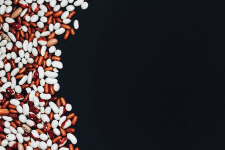 background with space for text. View from above. multi-colored beans scattered on a black background. brown and white beansの写真素材