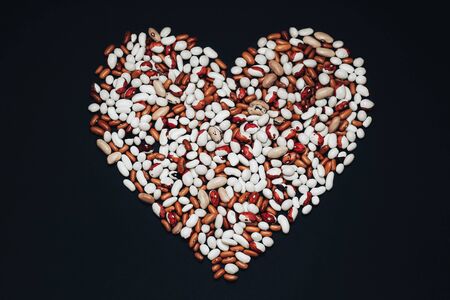Multicolored beans in the shape of a heart on a black background. brown and white beansの写真素材