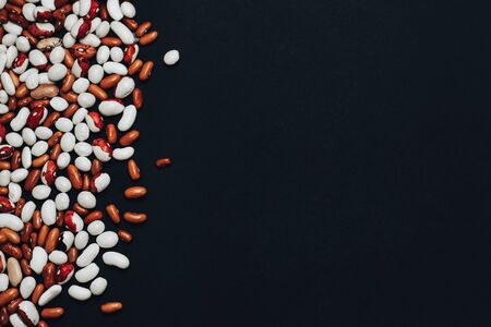 background with space for text. View from above. multi-colored beans scattered on a black background. brown and white beansの写真素材