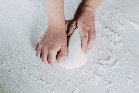 Making dough by female hands on white wooden table background. Female baker preparing bread dough at white table.の写真素材