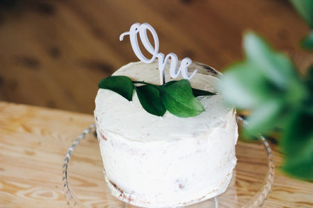 naked cake decorated with a sprig of greens and a wooden inscription one. cake for 1 year to the...