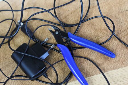 tangled charger wires. Black wire on a wooden background with blue nippersの写真素材