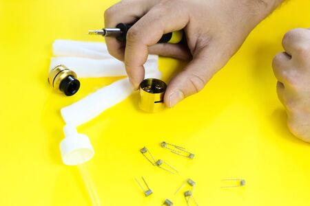 electronic cigarette details, Vata, coils, drip, spring, nippers on a yellow background. man's hands take apart vapeの写真素材