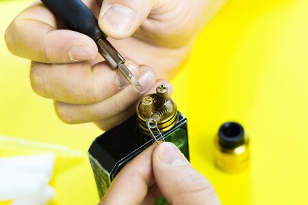 electronic cigarette details, Vata, coils, drip, spring, nippers on a yellow background. man's hands change springs in vapeの写真素材