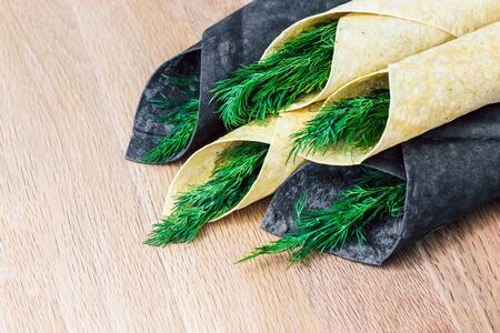 thin pita bread white and black rolled up in a straw with greens. Chorny pita with cuttlefish ink and Armenian traditional pitaの写真素材