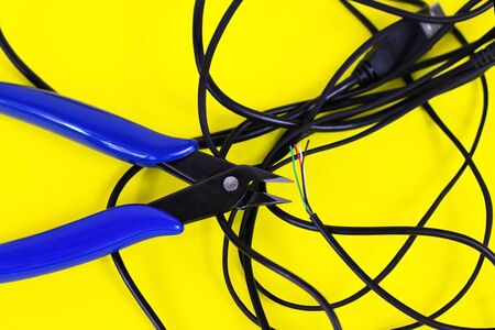 tangled charger wires. Black wire on a yellow background with blue nippersの写真素材