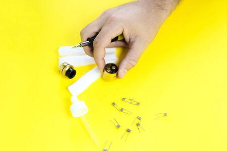 electronic cigarette details, Vata, coils, drip, spring, nippers on a yellow background. man's hands take apart vapeの写真素材