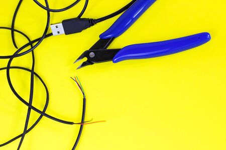 tangled charger wires. Black wire on a yellow background with blue nippersの写真素材