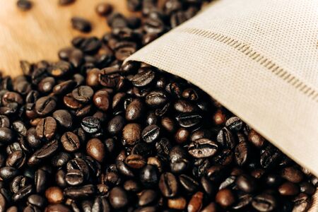 many coffee beans on a wooden background in an ecology bagの写真素材