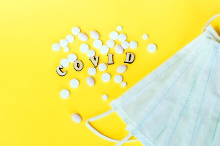 Wooden letters are lined with the word covid, pills with a medical mask. Concept on the theme of flu, virus.の写真素材