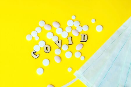 Wooden letters are lined with the word covid, pills with a medical mask. Concept on the theme of flu, virus.の写真素材