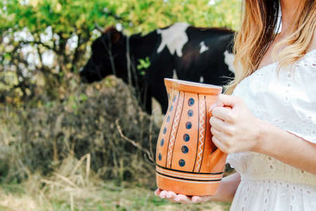 The girl is holding a jug of fresh milk. Against the background, a cow grazes in the fresh air.の写真素材