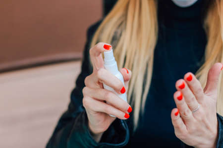a blonde girl with a red manicure treats her hands from germs with a sanitizerの写真素材