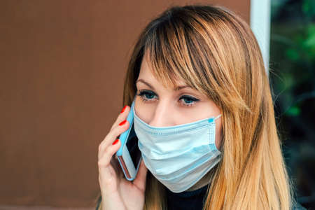 blonde girl with red manicure talking on the phone. Girl in medical mask.の写真素材
