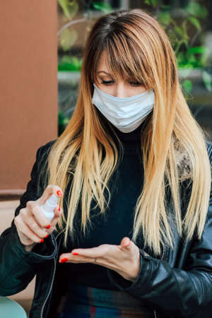 a blonde girl with red manicure treats the phone with a sanitizer from germs. Girl in medical mask.の写真素材