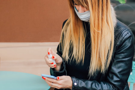a blonde girl with red manicure treats the phone with a sanitizer from germs.の写真素材