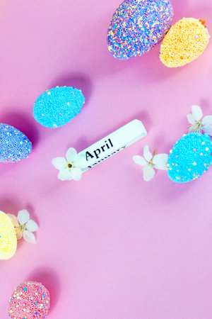 April lettering with Easter eggs and spring flowers on a pink background. Vertical flatley.
