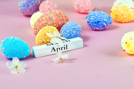 April lettering with Easter eggs and spring flowers on a pink background