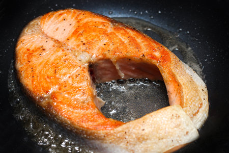 Salmon is fried in a black non-stick skillet. Cooking red fish.の写真素材