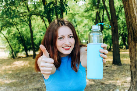 A girl with red hair rejoices and holds water in glass bottle.の写真素材