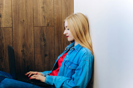 Girl with blond hair and blue eyes sits with a laptop.