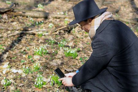 The girl on the phone photographs snowdrops in a clearing in the forest.の写真素材