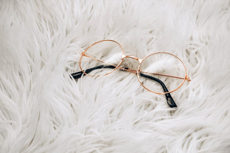 Reading glasses with gold frames on a white wool background.の写真素材