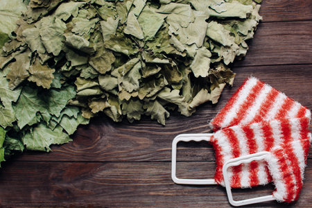 Two oak deciduous brooms for a bath with a washcloth on a wooden background.