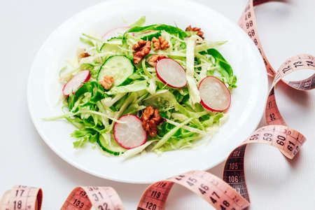 Cucumber salad with radishes, cabbage and nuts on a white plate and a centimeter. Top view on gray background.の写真素材