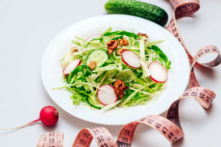 Cucumber salad with radishes, cabbage and nuts on a white plate and a centimeter. Top view on gray background.の写真素材