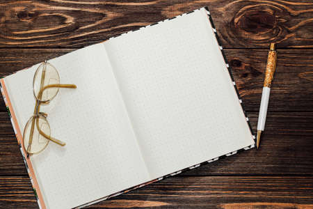 Notepad with reading glasses and a gold pen on a wooden table. Space for text.の写真素材