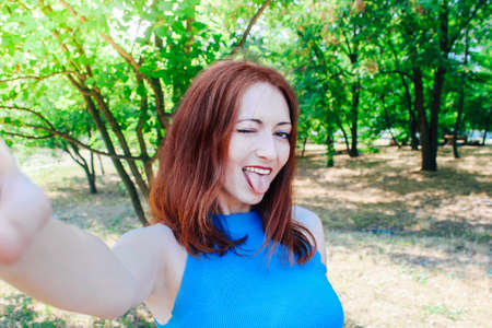 Young pretty girl with red hair takes a selfie on her phone in summer.の写真素材