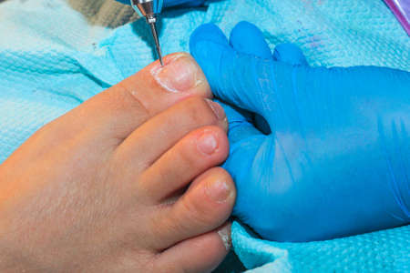 A gloved handler prepares the nail plate of the toe for gel coating.の写真素材