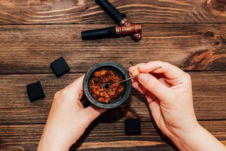 Clay bowl for hookah with coconut coals, wooden mouthpieces on a wooden background top view. Girl fills smoking tobacco.の写真素材