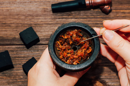 Clay bowl for hookah with coconut coals, wooden mouthpieces on a wooden background top view. Girl...