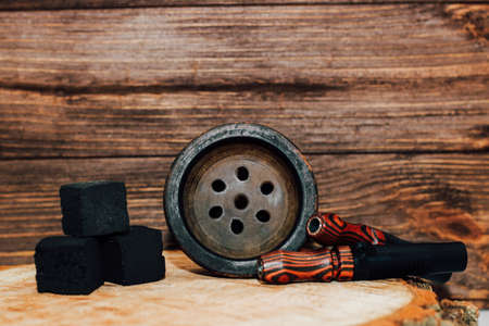 Clay bowl for hookah with coconut coals, wooden mouthpieces stands on a wooden background.の写真素材