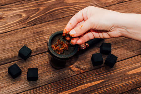 Clay bowl for hookah with coconut coals, wooden mouthpieces on a wooden background top view. Girl fills smoking tobacco.の写真素材