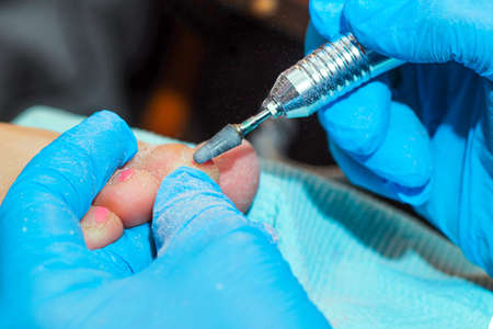 A gloved handler prepares the nail plate of the toe for gel coating.の写真素材