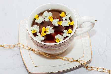 A beautiful white cup with a gold border, decorated with flowers and gold jewelry. Business account design.の写真素材