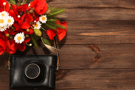 A bouquet of wildflowers: daisies and poppies on a wooden background with a camera. Place for text.