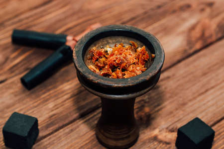 Clay bowl for hookah with coconut coals, wooden mouthpieces on a wooden background top view. Girl fills smoking tobacco.の写真素材