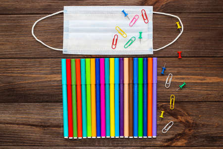 School creative flatley. Multi-colored markers and a medical protective mask lie on a wooden table.の写真素材