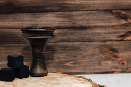 An earthenware bowl for a hookah with coconut coals stands on a wooden background.の写真素材