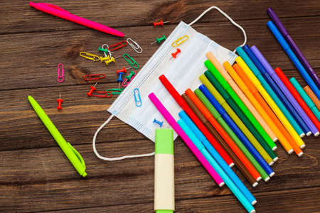 School creative flatley. Multi-colored paper clips with handles and a medical protective mask lie on a wooden table.の写真素材